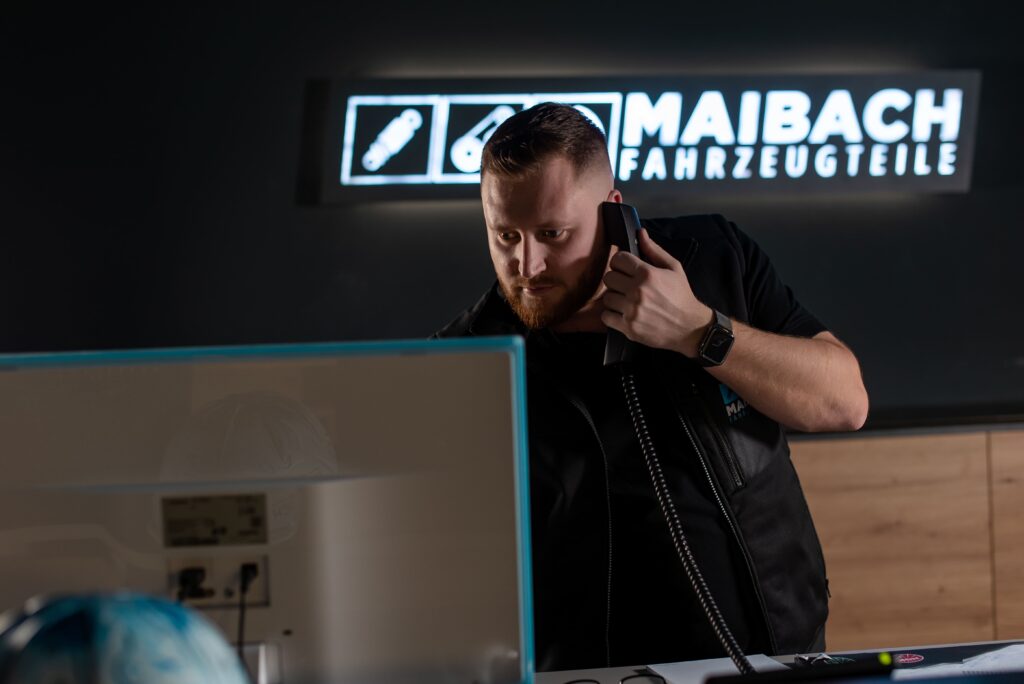 Ein Miarbeiter bei Maibach Fahrzeugteile im Service mit Telefonhörer in der Hand. Im Hintergrund Logo.